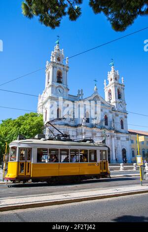 Eine ikonische gelbe Tram 28, die vor der Basilica da Estrela in Lissabon, der Hauptstadt Portugals, vorbeifährt. Stockfoto