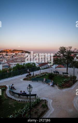 Touristen, die den Sonnenuntergang genießen und sich im Garten São Pedro de Alcântara entspannen, mit seinem Panoramablick auf das historische Zentrum von Lissabon, Portugal. Stockfoto