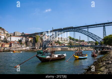 Schiffe auf dem Fluss Douro in der historischen Stadt Porto, mit der ikonischen Dom Luis Brücke im Hintergrund. Stockfoto