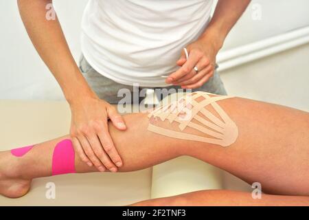 Junge Physiotherapeutin, die Kinesiologieband auf das Knie ihres Patienten anwendet, Nahaufnahme Detail auf den Händen Stockfoto