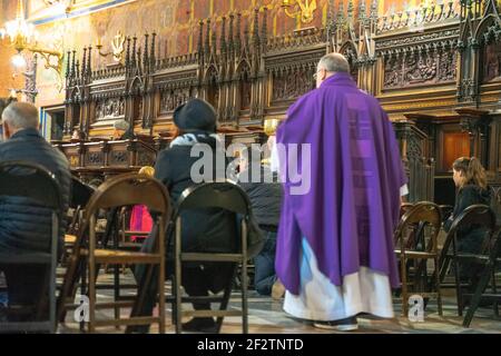 Priester in purpurfarbenem Mantel während der Zeremonie mit Kirchgängern oder Gemeindemitgliedern in der Basilika des Hl. Franziskus in Krakau, Polen Stockfoto