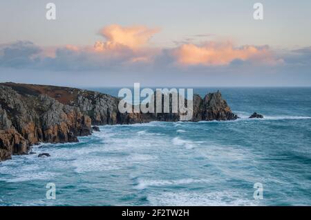 Sonnenuntergang über einer Meereslandschaft von Logan’s Rock und Pedn Vounder in Treen in West Cornwall mit einem interessanten, farbenfrohen, bewölkten Himmel. Stockfoto