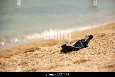 Schwarze Plastikflasche oder Müll am Strand des Meeres mit dem Hintergrund des Meeres und Licht der Sonne. Umweltkonzept. Recyceln Sie, um den globalen Krieg zu bekämpfen Stockfoto