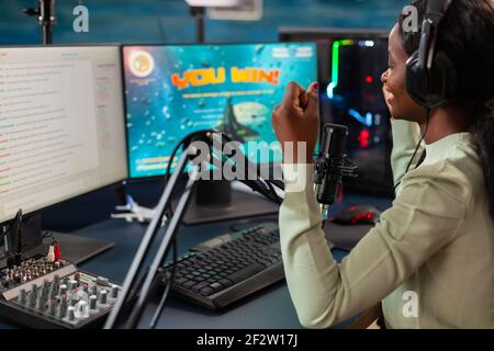 Professioneller Afro-esport-Spieler feiert den Sieg nach dem Sieg Meisterschaft. Online-Streaming Cyber-Performance während Videospiele Turnier in zu Hause mit Neonlicht. Stockfoto