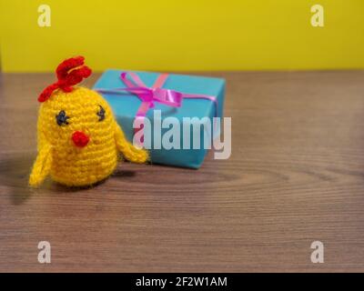 Spielzeug gelbe Huhn neben Geschenk in blauer Verpackung auf braunem Tisch. Stockfoto