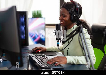 Lächelnd eSport streamer trägt Kopfhörer ejoying live competiton sitzen auf Stuhl. Streaming virale Videospiele zum Spaß mit Headset und Tastatur für Online-Meisterschaft. Stockfoto