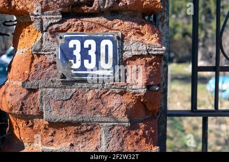 Nummer 330 Anzahl der Häuser Wohnungen Straßen. Die weiße Nummer der blauen Metallplatte Hausnummer dreihundert und dreißig (330) auf der Ziegelwand Stockfoto