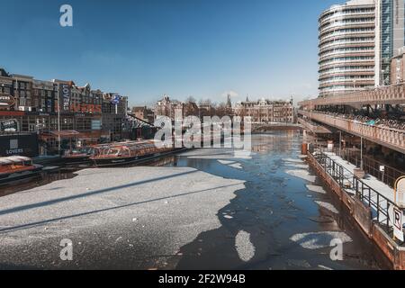 Amsterdam, Niederlande, 12. Februar 2021: Der gefrorene Kanal Oosterdok in der Altstadt von Amsterdam mit den wegen COVID angedockten Ausflugsbooten auf der le Stockfoto