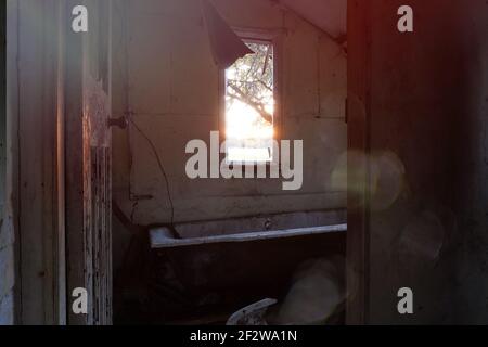 Blick aus einem Fenster auf den Sonnenuntergang in einem gespenstischen verlassenen Haus. Mit verfallenden Wänden und kaputter Badewanne. Mit einem Retro, Licht Lecks bearbeiten. Stockfoto