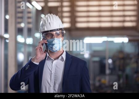 Mechaniker mit Maske sprechen am Telefon in einem Werk Stockfoto