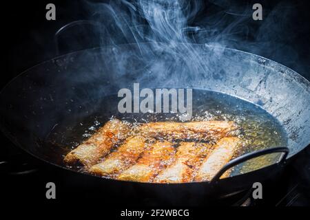 Frische Frühlingsrollen in schwarzem Wok braten. Vietnamesische Küche. Stockfoto
