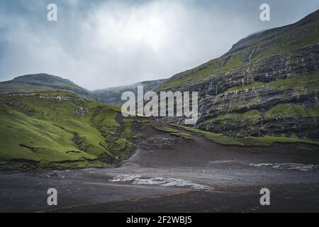 Flussdelta mit schwarzem Sandstrand, Felsen und hohen Klippen auf den Färöer Inseln, in der Nähe des Dorfes Saksun auf der faröischen Insel Streymoy während der Ebbe Stockfoto