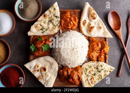 Flache Lay-Bild der traditionellen indischen Küche Platte auf dunklem Hintergrund mit Gewürzen und Kräutern auf der Seite. Das Sortiment enthält Naan-Brote sowie Stockfoto