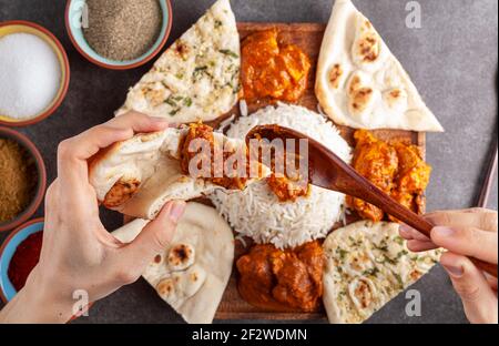 Flaches Lay-Bild einer Frau, die Huhn Tikka Masala auf eine Scheibe Naan-Brot mit einer Platte mit traditionellen indischen Speisen darunter. Gewürze und Kräuter Stockfoto