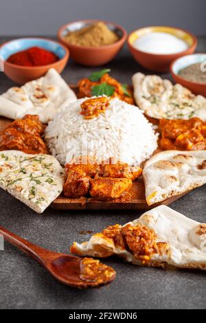 Angewinkeltes Bild einer Gourmet-Mischung aus indischen Gerichten wie Reis, Naan, Tikka Masala, Butterhuhn und Curry. Gewürze und Kräuter sind in verschwommen gesehen Stockfoto