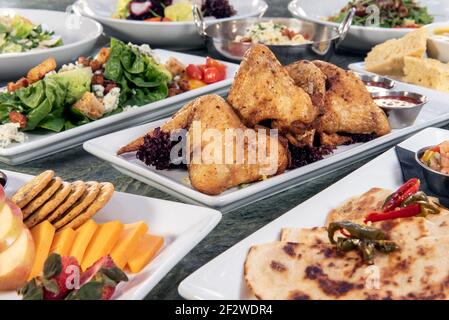 Voller Tisch mit einer Vielzahl von Restaurant-Gerichten zur Auswahl mit gebratenen Hähnchenflügeln in der Mitte. Stockfoto