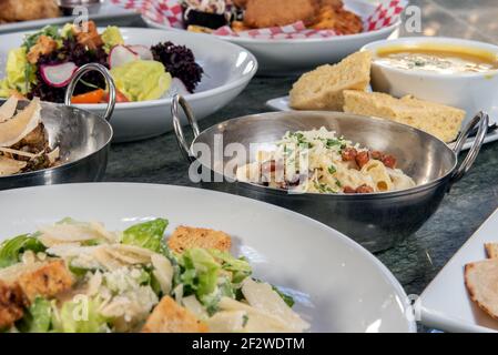 Voller Tisch mit einer Vielzahl von Restaurant-Gerichten zur Auswahl mit Makkaroni und Käseschale in der Mitte. Stockfoto