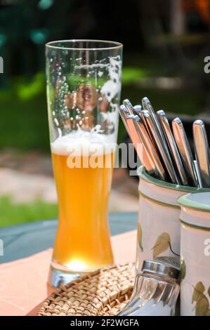 Ein halb leeres Weißbierglas auf dem Tisch in einem Biergarten, mit Besteck in Bierkrügen. Machen Sie eine Pause bei einer Wanderung an einem schönen Sommertag Stockfoto