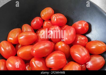 Nahaufnahme eines Stapels Kirschtomaten, frisch gewaschen, in einer schwarzen Eisenschüssel auf einem Metallwaschbecken. Stockfoto