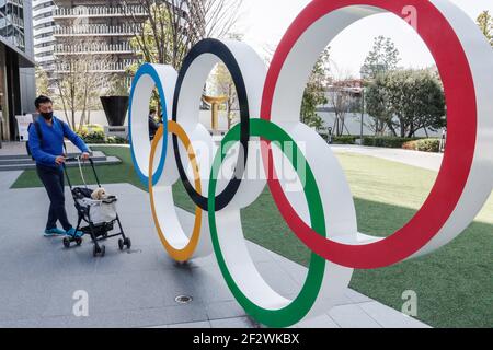 Tokio, Japan. März 2021, 11th. Ein Mann mit Gesichtsmast geht hinter die olympischen Symbole der fünf verschränkte Ringe in der Nähe des Nationalstadions in Tokio. Etwa 80% der Japaner in den letzten Umfragen sagen, dass die Olympischen Spiele verschoben oder abgesagt werden sollten, und fast so viele wollen keine Fans aus dem Ausland. (Foto von James Matsumoto/SOPA Images/Sipa USA) Quelle: SIPA USA/Alamy Live News Stockfoto