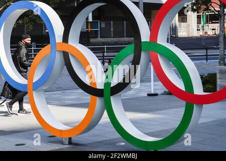 Tokio, Japan. März 2021, 11th. Ein Mann mit Gesichtsmast geht hinter die olympischen Symbole der fünf verschränkte Ringe in der Nähe des Nationalstadions in Tokio. Etwa 80% der Japaner in den letzten Umfragen sagen, dass die Olympischen Spiele verschoben oder abgesagt werden sollten, und fast so viele wollen keine Fans aus dem Ausland. Kredit: SOPA Images Limited/Alamy Live Nachrichten Stockfoto