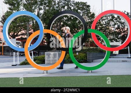 Tokio, Japan. März 2021, 11th. Ein Mann mit Gesichtsmast geht hinter die olympischen Symbole der fünf verschränkte Ringe in der Nähe des Nationalstadions in Tokio. Etwa 80% der Japaner in den letzten Umfragen sagen, dass die Olympischen Spiele verschoben oder abgesagt werden sollten, und fast so viele wollen keine Fans aus dem Ausland. Kredit: SOPA Images Limited/Alamy Live Nachrichten Stockfoto