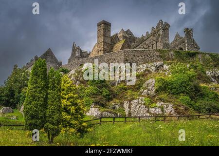 Bäume und Wiese am Fuße des Rock of Cashel, bekannt als Cashel of Kings oder St. Patricks Rock mit dramatischen Sturmwolken, Grafschaft Tipperary, Irland Stockfoto