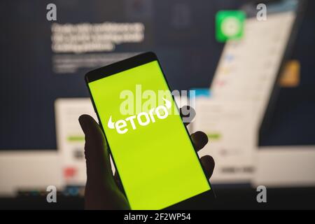 Mann hält ein Smartphone mit eToro Logo mit verschwommener Website als Hintergrund. Handelsplattform, Investitionen in Aktien und Kryptowährungen Stockfoto