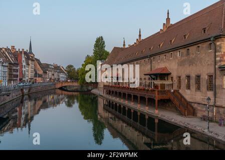 Blick auf den Sonnenuntergang über der Uferpromenade eines Kanals, der das Gebäude ancienne douanne in Straßburg, Frankreich, passiert Stockfoto