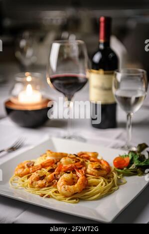 Pasta mit Knoblauch Garnelen und Olivenöl auf einem weißen Teller am Tisch, mit einem Glas und eine Flasche Wein im Hintergrund. Stockfoto