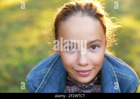 Schöne Teenager-Mädchen mit glücklichen Gesichtsausdruck Blick auf die Kamera mit Freude. Nahaufnahme. Vorderansicht. Fröhliches Kind im Freien Stockfoto