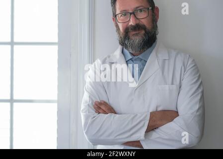 Portrait von lächelnden jungen kaukasischen männlichen Arzt tragen weiße medizinische Uniform, Stethoskop und Brille Blick auf Kamera posiert in Privatklinik, glücklicher Mann Stockfoto
