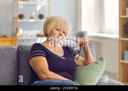 Porträt einer positiven älteren Frau oder Großmutter im T-Shirt sitzend Auf Sofa mit Brille Stockfoto