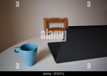 Ein blauer Becher und ein Laptop auf einem Tisch mit Ein Holzstuhl in einem Zimmer Stockfoto