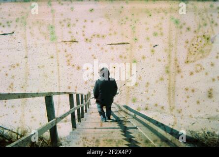 Beschädigtes und verschwommenes Foto mit Mann auf der Treppe mit Flecken und Kratzern. Vintage Distressed Foto. Stockfoto