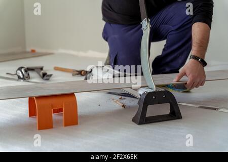 Geschlossene Aufnahme eines Mannes, der ein Blatt Holz schneidet Mit einer Guillotine für die Installation eines Holzbodens Stockfoto