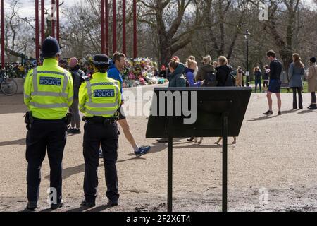 Polizist und Frau beobachten, wie Menschen Blumengebete auf Clapham Common in Erinnerung an Sarah Everard, entführte und ermordete , London, England, legen