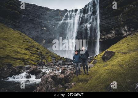 Junger männlicher Tourist, der vor dem Fossa Wasserfall auf der Insel Bordoy steht. Dies ist der höchste Wasserfall auf den Färöer Inseln, in Stockfoto