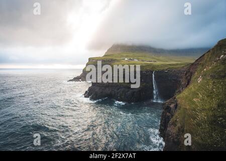 Luftdrohne Ansicht von Gasadalur Dorf und Mulafossur seinen ikonischen Wasserfall, Vagar, Färöer Inseln, Dänemark. Raue See im nordatlantik Ozean. Üppig Stockfoto