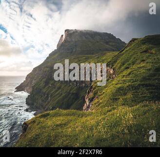 Färöer-Inseln mit stürmischer Sicht auf Tindholmur und Drangarnir auf der Insel Vagar vom Mulafossur-Wasserfall aus gesehen. Niedrige Wolken mit atlantik Stockfoto