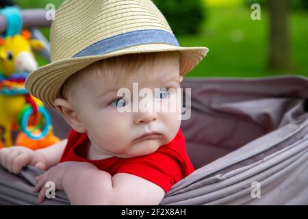 Cute Baby Junge trägt einen Hut sitzen Blick aus der Seite seines stollers Stockfoto