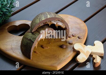 Ein halbes geschnittenes Osterei (Ovo de Pascoa), mit doppelter Schale gefüllt mit geschmolzenem Karamell und Keks, verziert mit essbarer Goldfarbe, neben Choco Stockfoto