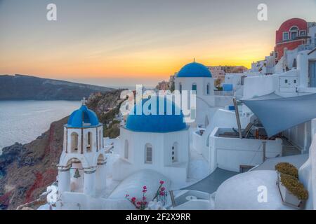 Blick auf den Sonnenuntergang auf Kirchen und blaue Kuppeln von Oia Stadt in Santorini, Griechenland Stockfoto