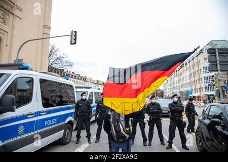 Demonstrant stellt sich vor einer Absperrung des USK und hält Deutschland Flagge mit Aufschrift: ' Merkel muss weg '. Am 13. März 2021 sammeln sich tausend Menschen in München, um gegen sämtliche Covid Maßnahmen zu demontieren. Eine Demonstration vom Königsplatz gestartet wurde vom Versammlungsleiter Markus Haintz abgeschlossen, weil die Polizei die Teilnehmerbeschränkung durchlief. Die Kundgebung am Maxmonument überschritt die 500 erlaubte Teilnehmer*innen deutlich. Viele trugen keine Mask or trugen sie not right. * am 13 2021. März versammelten sich mehrere Tausend Menschen in München, G Stockfoto