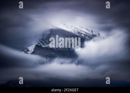 Die Wolkenbewegung, die an einem dunklen, launischen Morgen um den Gipfel des Mount Rundle in den kanadischen Rockies wirbelt. Stockfoto