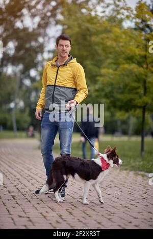 Junger kaukasischer Rüde, der seinen Hund an der Leine hereinläuft Wunderschöner Herbstpark Stockfoto