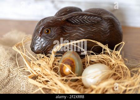 Ostereier aus dekorativem Marmorstein auf einem Strohnest und ein glücklicher Hase aus handgefertigtem Holz zur Unterhaltung kleiner Kinder. Stockfoto