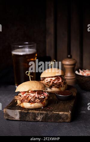 Leckere Hamburger mit Schweinefleisch und Krautsalat in knuspriger Form Brötchen auf rustikalem Holzbrett serviert Stockfoto