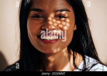 Attraktive, fröhliche junge hispanische Frau mit weißem Tuch, die im Schatten der Sonne die Kamera anschaut Stockfoto