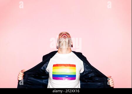 Selbstbewusster bärtiger Mann mit roten Lippen, der schreit und LGBT vorführt Flagge auf weißem T-Shirt auf rosa Hintergrund Stockfoto